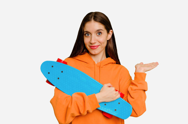 junge Skater kaukasische Frau isoliert zeigt eine Kopie Raum auf einer Handfläche und hält eine andere Hand auf der Taille. - Foto, Bild