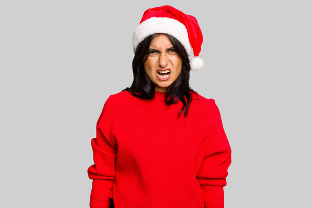 Young Indian woman celebrating Christmas wearing a santa hat isolated screaming very angry and aggressive. - Photo, image