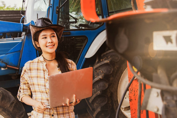 Asian woman farmer smile, agribusiness and livestock operator holding laptops to inspect machines and tractors for agricultural use, inspect maintenance services and use on agricultural plantations. - Φωτογραφία, εικόνα