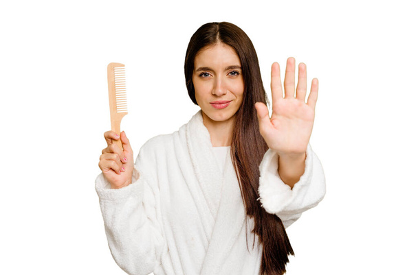 Νεαρή καυκάσια γυναίκα κρατώντας μια χτένα μαλλιών απομονωμένη στέκεται με απλωμένο χέρι δείχνει στοπ, εμποδίζοντας σας. - Φωτογραφία, εικόνα