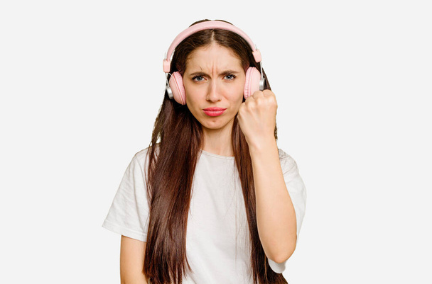 Mladá běloška nosí sluchátka izolované ukazující pěst na kameru, agresivní výraz obličeje. - Fotografie, Obrázek