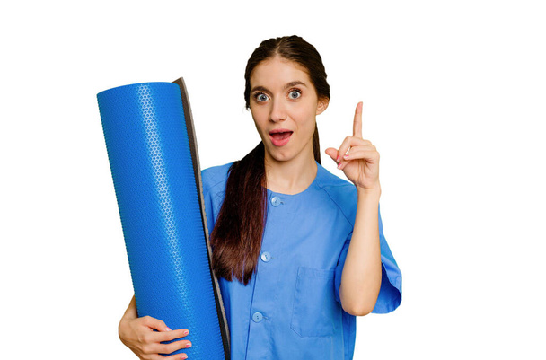 Young caucasian physiotherapist woman holding a mat isolated having an idea, inspiration concept. - Foto, Bild