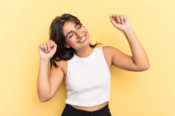 Young Indian woman isolated on yellow background celebrating a special day, jumps and raise arms with energy. - Photo, Image