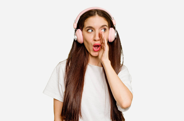Junge kaukasische Frau trägt Kopfhörer isoliert sagt eine geheime heiße Bremsnachrichten und schaut zur Seite - Foto, Bild