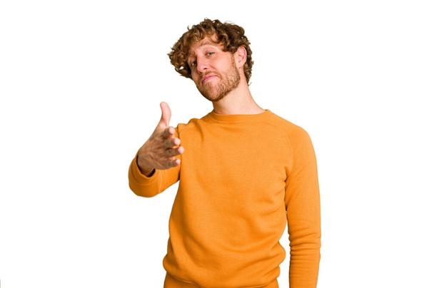 Young caucasian man isolated on green chroma background stretching hand at camera in greeting gesture. - Photo, Image