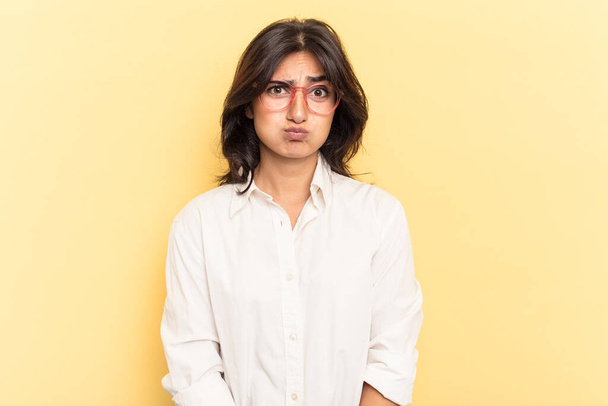 Jonge Indiase vrouw geïsoleerd op gele achtergrond blaast wangen, heeft vermoeide uitdrukking. Gezichtsuitdrukking. - Foto, afbeelding