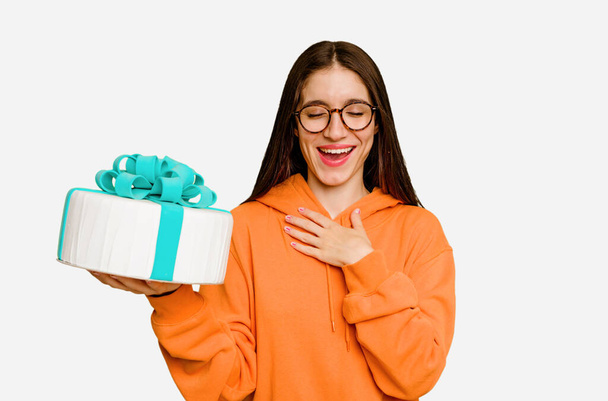 Young caucasian woman holding a birthday cake isolated laughs out loudly keeping hand on chest. - Photo, Image