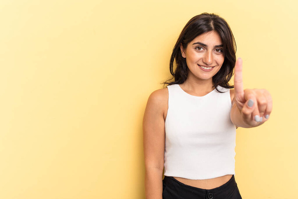 Young Indian woman isolated on yellow background showing number one with finger. - Photo, image