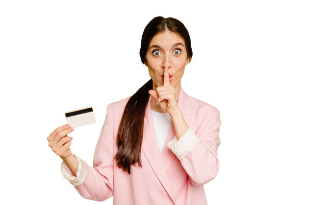 Business caucasian woman holding a credit card isolated keeping a secret or asking for silence. - Foto, afbeelding