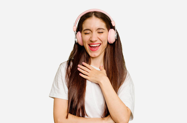 Mladá běloška nosí sluchátka izolované směje se hlasitě držet ruku na hrudi. - Fotografie, Obrázek
