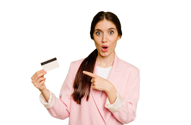 Mulher caucasiana de negócios segurando um cartão de crédito isolado apontando para o lado - Foto, Imagem