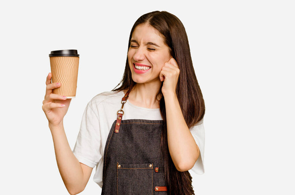 Νεαρή μπαρίστα που κρατάει τον καφέ, απομονωμένη καλύπτοντας αυτιά με τα χέρια.. - Φωτογραφία, εικόνα