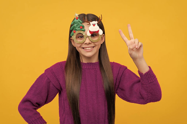 xmas holiday decoration. childhood concept. peace. merry christmas. happy new year. happy child having fun. kid with party glasses. teen girl on yellow background. - Photo, Image