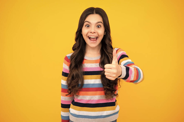 Amazed teenager. Excited teen girl. Happy casual teenager child girl showing thumb up and smiling isolated on yellow background - Photo, Image