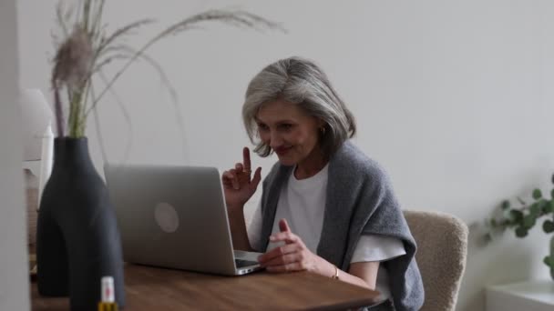 Dojrzała pięćdziesięcioletnia kobieta w stylowych ubraniach w domu komunikuje się przez łącze wideo na laptopie ze swoimi wnukami i dziećmi. - Materiał filmowy, wideo