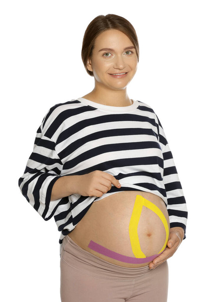 妊娠女性とともにkinesioテープオン彼女の腹に白の背景 - 写真・画像