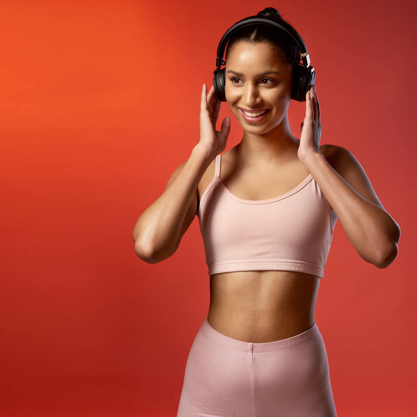 Listening to music can enhance your performance. Studio shot of a sporty young woman listening to music against a red background - Photo, Image
