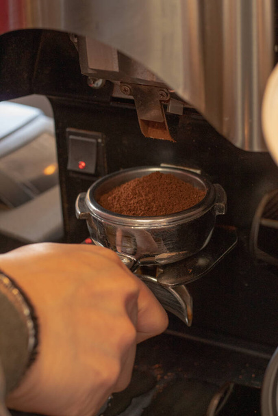 Zblízka baristova ruka držící portafilter naplněný mletou kávou před kávovarem na espresso - Fotografie, Obrázek