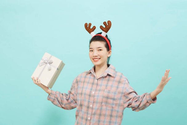 Mujer asiática linda alegre sosteniendo una caja de regalo con una tarjeta de crédito sobre fondo de color azul brillante. Navidad y año nuevo concepto de alegría de ventas - Foto, Imagen