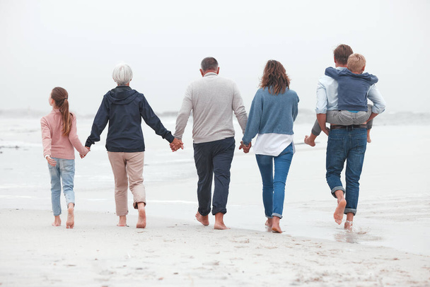 Tomados de la mano, caminando y gran familia en la playa para hacer ejercicio durante las vacaciones de verano. Abuelos, padres e hijos en caminata al aire libre en la naturaleza por el océano mientras están de vacaciones, aventura o viaje - Foto, imagen