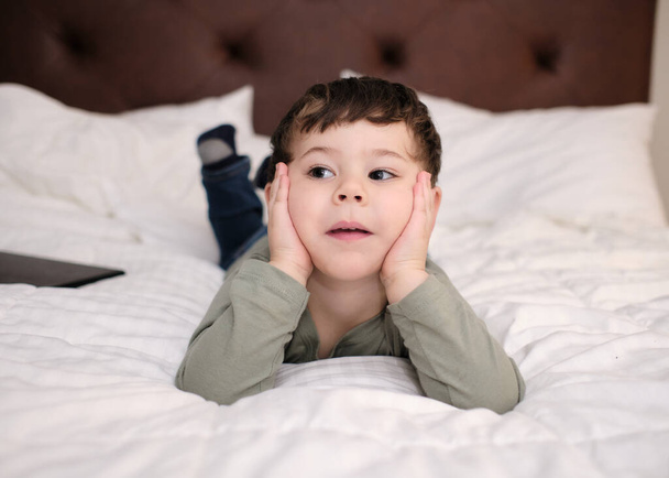 expresivní mladý chlapec sledování televize na posteli v hotelovém pokoji - Fotografie, Obrázek