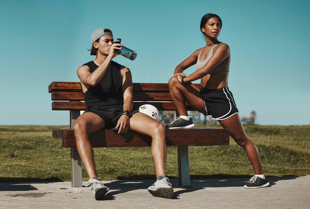 Sports, bench and fitness people with water bottle in a park for outdoor training, workout or wellness with blue sky mock up. Athlete or runner couple relax together after running with summer mockup. - Photo, Image