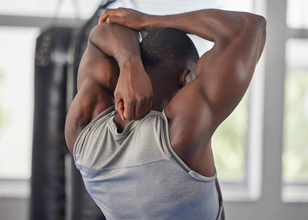 Fitness, bodybuilder and black man stretching at gym for training, exercise and workout for strong powerful muscles. Back view, sports and healthy athlete starting biceps, triceps and elbow warm up. - Fotografie, Obrázek