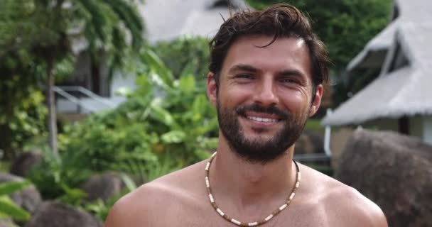 Atractivo hombre macho con el torso desnudo sobre la naturaleza tropical, disfruta tomando el sol, sonriendo hermosa sonrisa dentada. Cabeza disparada - Metraje, vídeo