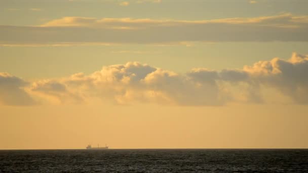 Zaman ayarlı. Denizdeki ufuk çizgisinde tahıl taşıyıcı tanker silueti ve gün batımında sarı mavi gökyüzünde hızlı hareket eden bulutlar. Deniz manzarası, deniz manzarası. Ulaşım. Doğal arkaplan - Video, Çekim