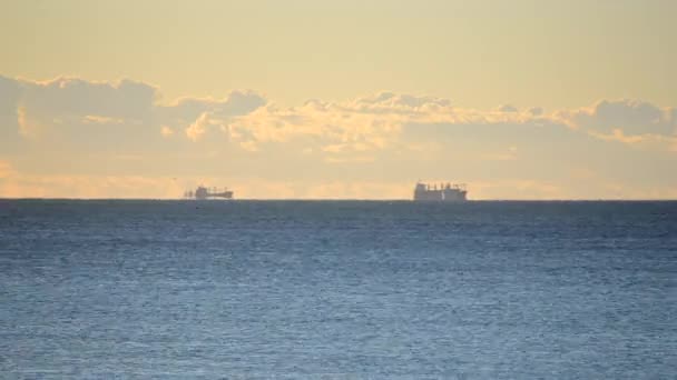 Denizdeki ufuk çizgisinde tanker tankerlerinin silueti ve gün batımında sarı mavi gökyüzünde hızlı hareket eden bulutlar. Deniz manzarası, deniz manzarası. Ulaşım. Doğal arkaplan - Video, Çekim