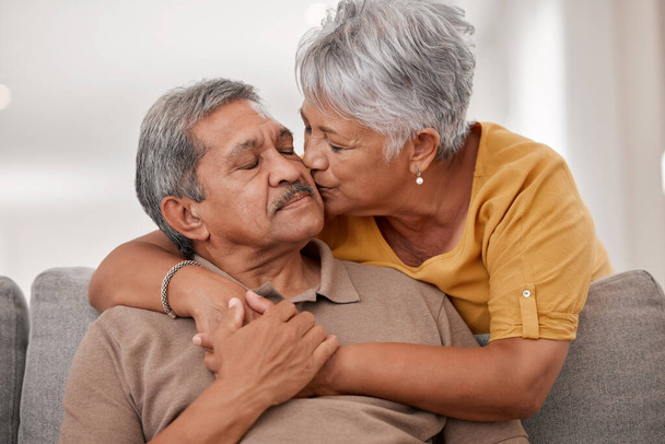 Küsschen, Liebe und Seniorenpaar im Wohnzimmer ihres Hauses während des gemeinsamen Ruhestands. Glücklicher, liebevoller und älterer Mann und Frau mit Zuneigung, Unterstützung und Hilfe in der Ehe auf dem heimischen Sofa. - Foto, Bild