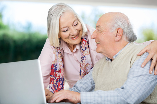 Lächelndes Senioren-Paar schaut sich mit Laptop an - Foto, Bild