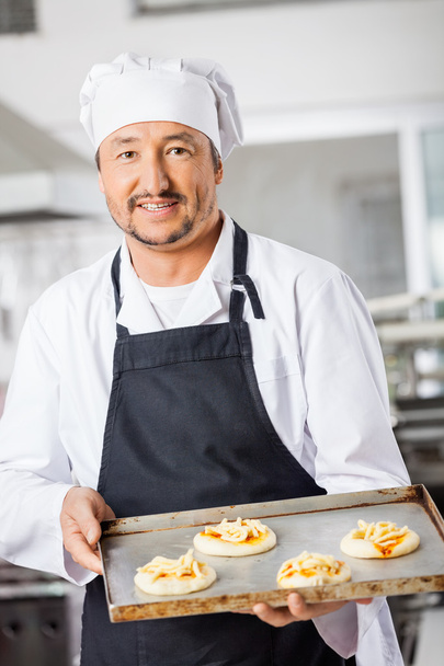 Confident Chef Holding Small Pizzas On Baking Sheet In Kitchen - Photo, image