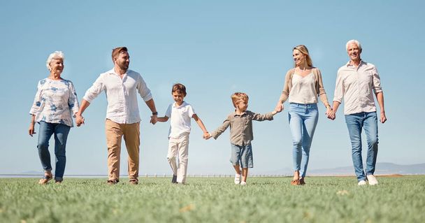 Family, love and walking with smile, together and happy on a field in nature with a blue sky background. Big family with kids, parents and grandparents enjoy weekend, holiday and summer in Germany. - Photo, Image