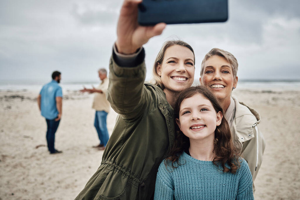 Telefon, selfie ve plaj bir kız, anne ve büyükanne tatildeyken deniz kenarında fotoğraf çekiyorlar. Yaz, teknoloji ve kadın akrabalarla aşk bir resim için poz. - Fotoğraf, Görsel