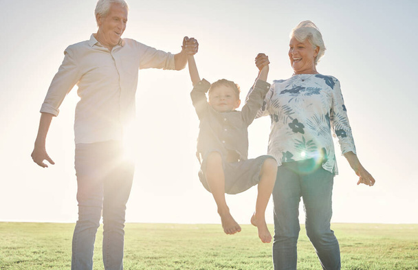 Family, holding hands and grandparents with boy in park, nature or outdoors. Love, support and happy man and woman lift child, kid and having fun time, care or bonding with smile together in sunshine. - Фото, зображення