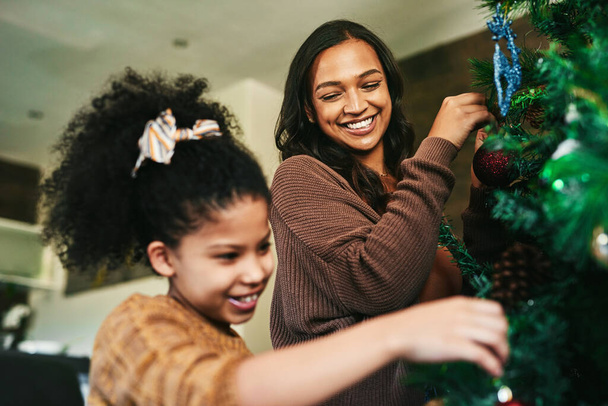ママと私だけで木をトリミング。幸せな若い母親と娘がクリスマスツリーを家で飾り - 写真・画像
