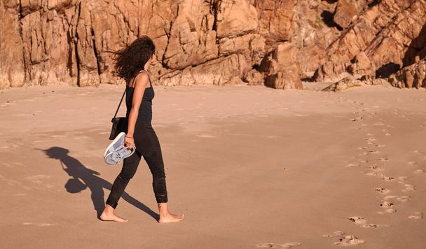 Si vous n'explorez pas, vous ne découvrirez jamais les joyaux cachés de la nature. une femme tenant ses chaussures lors d'une promenade sur la plage - Photo, image
