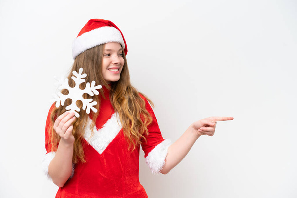 Mladá běloška žena s vánočními šaty drží sněhovou vločku izolované na bílém pozadí ukazuje na stranu prezentovat produkt - Fotografie, Obrázek
