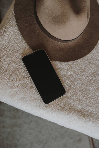 Mobile phone on chair with elegant hat. Flat lay, top view. Aesthetic copy space mockup template. - Photo, Image