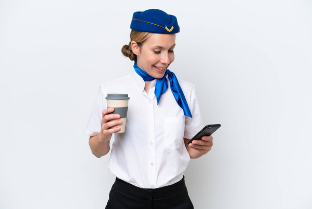 Αεροπλάνο ξανθιά αεροσυνοδός γυναίκα απομονωμένη σε λευκό φόντο κρατώντας καφέ για να πάρει μακριά και ένα κινητό - Φωτογραφία, εικόνα