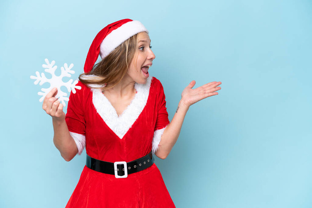 Anne Noel Baba gibi giyinmiş beyaz bir kadın elinde kar tanesiyle mavi arka planda, sürpriz bir yüz ifadesiyle izole edilmiş. - Fotoğraf, Görsel
