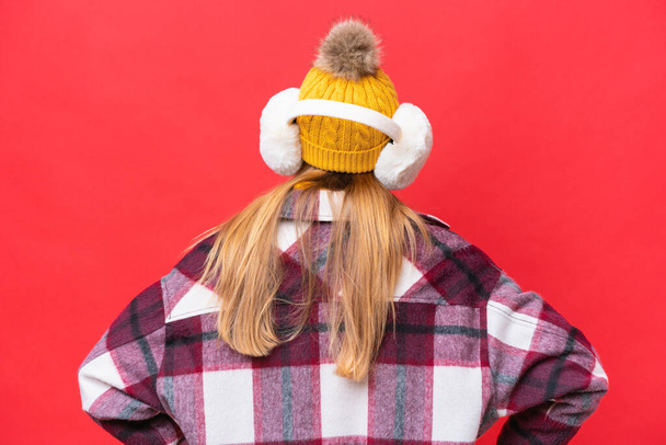 Jovem mulher bonita vestindo regalos de inverno isolado no fundo vermelho na posição traseira - Foto, Imagem