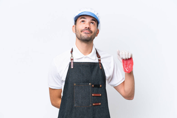 Butcher caucasian man wearing an apron and serving fresh cut meat over isolated white background and looking up - Foto, imagen