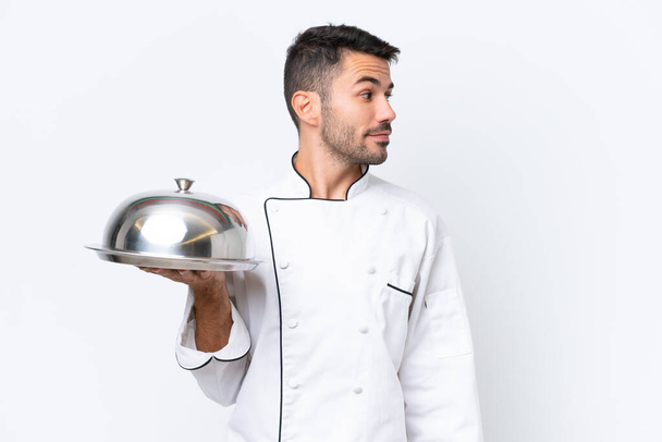 Fiatal szakács tálcával elszigetelt fehér háttér néz oldalra - Fotó, kép