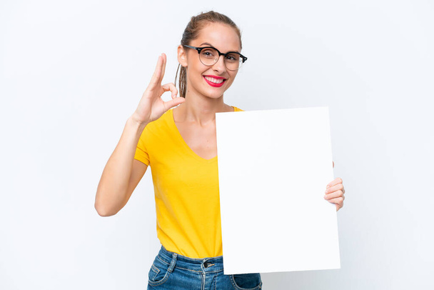 Fiatal kaukázusi nő elszigetelt fehér háttér kezében egy üres plakát és csinál OK jel - Fotó, kép
