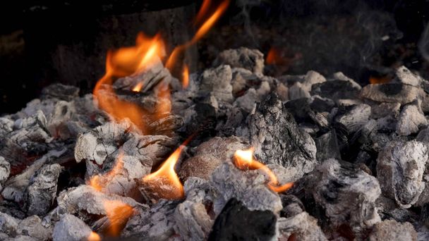 Petites flammes de feu sortant des cendres chaudes du barbecue et du charbon de bois - Photo, image