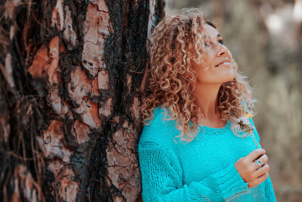 Portrait latéral de la femme souriant et profitant de la nature dans les loisirs de plein air. Femmes touristes contre un tronc d'arbre, sourire et admirer l'environnement naturel autour. Concept de voyage et de bonheur - Photo, image
