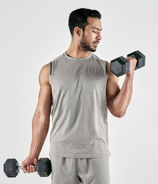 Difficult weights lead to amazing gains. Studio shot of a muscular young man exercising with dumbbells against a white background - 写真・画像