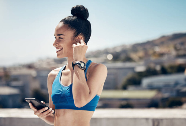 Fitness, music and woman athlete on a phone on rooftop for sports workout or exercise in city. Training, smile and happy girl from Mexico networking on social media with smartphone on balcony in town. - Photo, Image